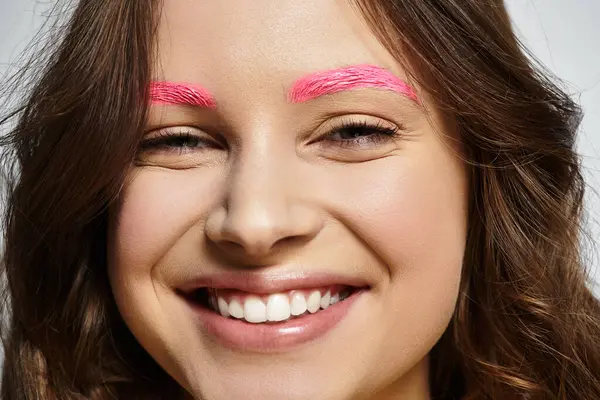 Junge Frau präsentiert ihre auffälligen rosa Augenbrauen und ihren selbstbewussten Stil vor grauem Hintergrund. — Stockfoto