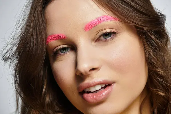 Eine junge Frau präsentiert ihre einzigartige Schönheit und leuchtend rosa Augenbrauen vor grauem Hintergrund. — Stockfoto