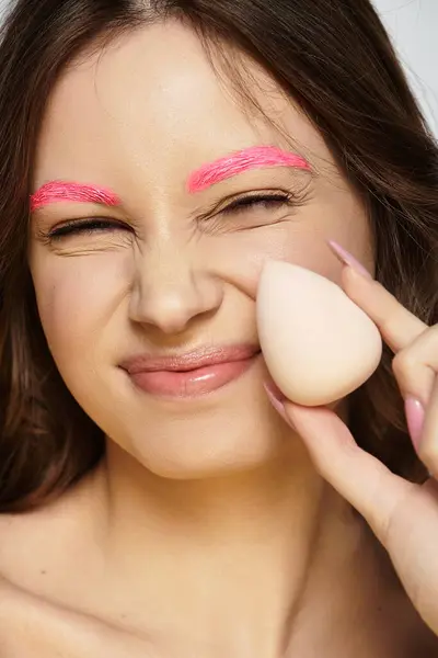 Young woman showcases her unique style with bold pink eyebrows on a grey background. — Stock Photo