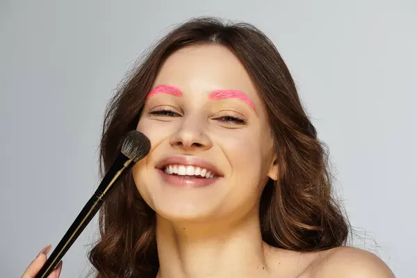 Cheerful young woman showcases her vibrant pink eyebrows against a grey backdrop. — Stock Photo