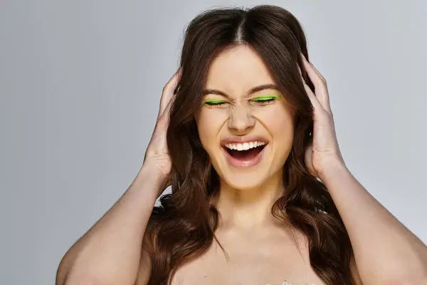Una joven sonríe alegremente, haciendo alarde de audaz sombra de ojos verde sobre un fondo gris. — Stock Photo