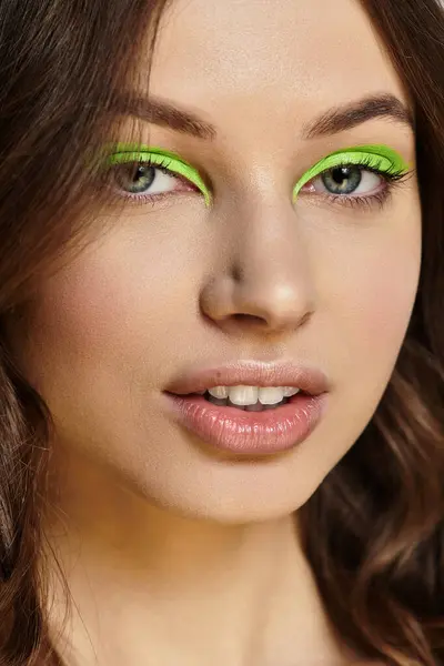 Young woman confidently showcases her striking green eyeshadow against a neutral backdrop. — Stock Photo