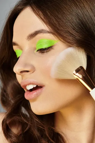 La sombra de ojos verde y vibrante realza la belleza juvenil de una mujer en un fondo de estudio gris. — Stock Photo