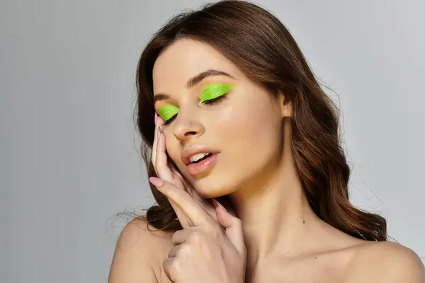 Attractive young woman elegantly poses with bright green eyeshadow against a grey backdrop. — Stock Photo