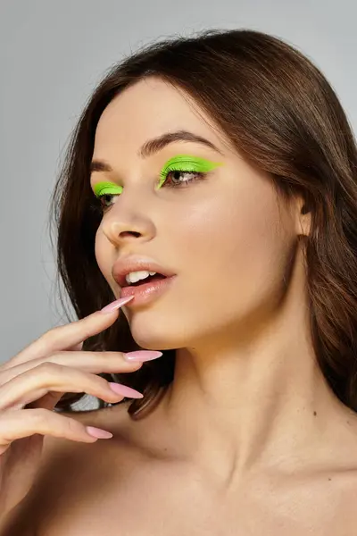 Young woman showcases an artistic makeup look with bright green eyeshadow and styled hair. — Stock Photo