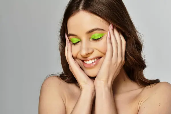 Attractive young woman showcases bold makeup with striking green eyeshadow in studio lighting. — Stock Photo