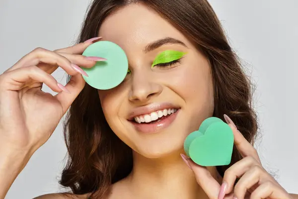 Attraktive junge Frau präsentiert ihr lebendiges Make-up mit grünem Lidschatten vor grauem Hintergrund. — Stockfoto