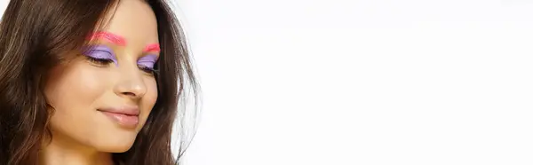 A young woman showcases bold makeup with vibrant purple eyeshadow and pink brows on grey, banner — Stock Photo