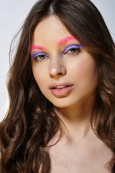 A young woman showcases striking makeup artistry with bold pink eyebrows and purple eyeshadow. — Stock Photo