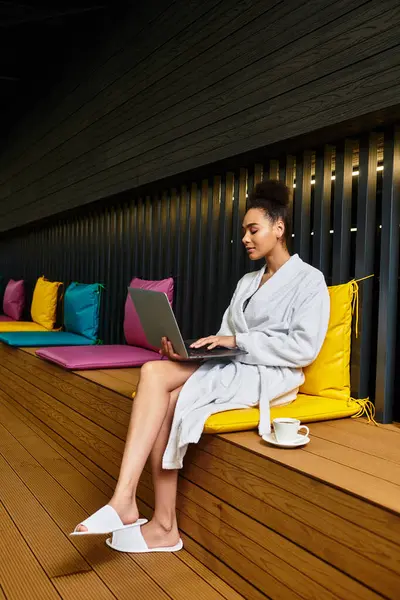 A young chic woman in a spa gown enjoys tea while working on her laptop. — Stock Photo