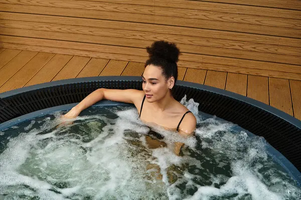 Une jeune afro-américaine se détend dans un bain bouillonnant dans un spa paisible. — Photo de stock