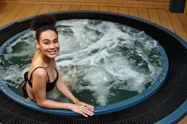 A young african american woman smiles joyfully while enjoying a soothing soak in warm waters. — Stock Photo