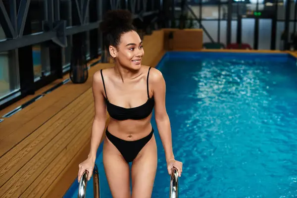 A young African American woman smiles while stepping into a spa pool, embracing relaxation and joy. — Stock Photo