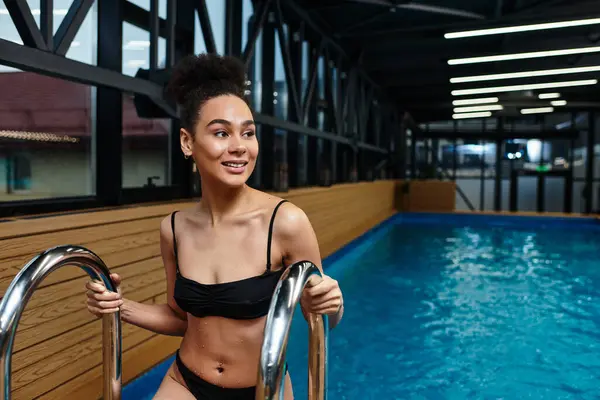 A beautiful young African American woman smiles as she ascends from the soothing waters of a spa. — Stock Photo