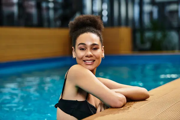 A young african american woman relaxes by the serene waters of a spa, enjoying carefree moments. — Stock Photo