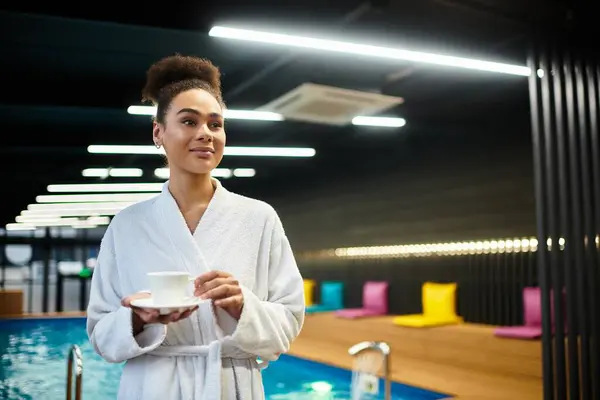A beautiful young woman in a robe holds a cup while soaking in the calming atmosphere of a spa. — Stock Photo