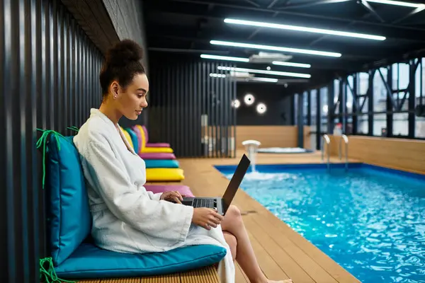 A young woman relaxes in a robe, focusing on her laptop as she enjoys the tranquil spa ambiance — Stock Photo