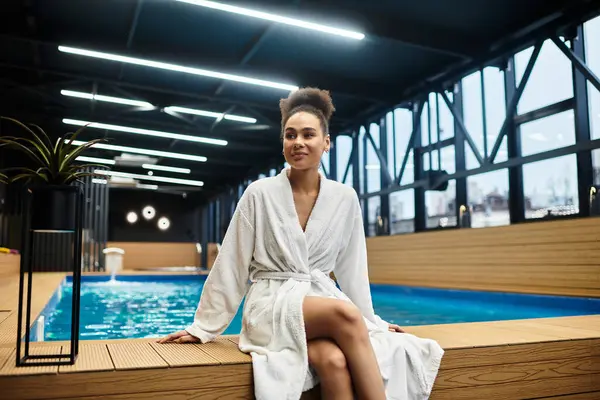 A young African American woman in a robe enjoys relaxation by the poolside in a spa. — Stock Photo