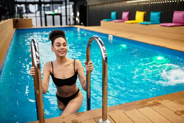 A young african american woman smiles while entering a serene spa pool, embracing relaxation. — Stock Photo