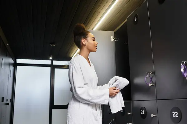 En un sereno spa, una joven afroamericana sonríe mientras sostiene una toalla, lista para relajarse. - foto de stock