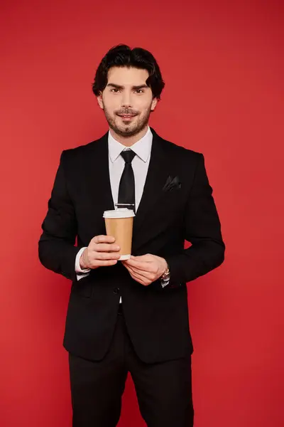 Stylish man in a tailored suit enjoys a warm drink, surrounded by a striking red backdrop. — Stock Photo