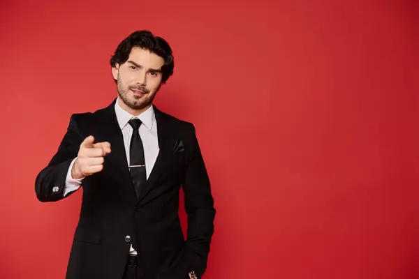 A young man with dark hair, dressed in a sleek black suit, striking a confident pose while smiling. — Stock Photo