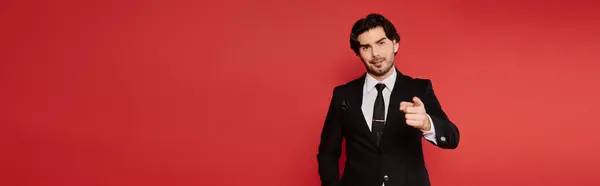 A young, stylish man in a tailored suit stands against a bright red background, exuding charisma. — Stock Photo