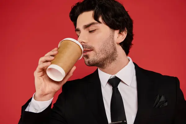 Brunette man enjoys a warm cup of coffee while dressed sharply in a black suit, exuding confidence. — Stock Photo