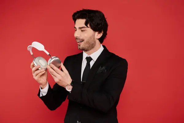 A young man in a sleek suit examines his modern headphones with excitement, exuding charm and style. — Stock Photo