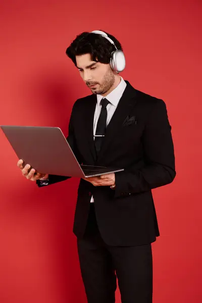 Handsome young man focused on his laptop while wearing headphones, surrounded by vivid red colors. — Stock Photo