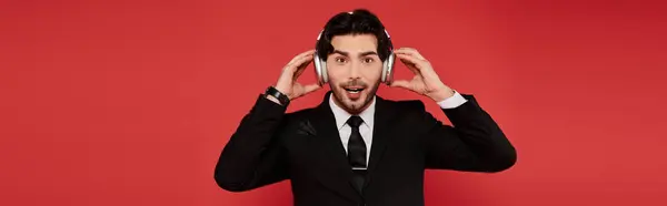 Handsome young man in a suit expresses excitement while listening to music on headphones. — Stock Photo