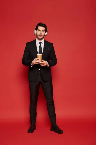 A young, handsome man dressed in a suit holds a coffee cup while wearing headphones. — Stock Photo