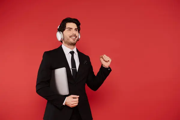 A stylish young man dances joyfully to music while holding his laptop. — Stock Photo