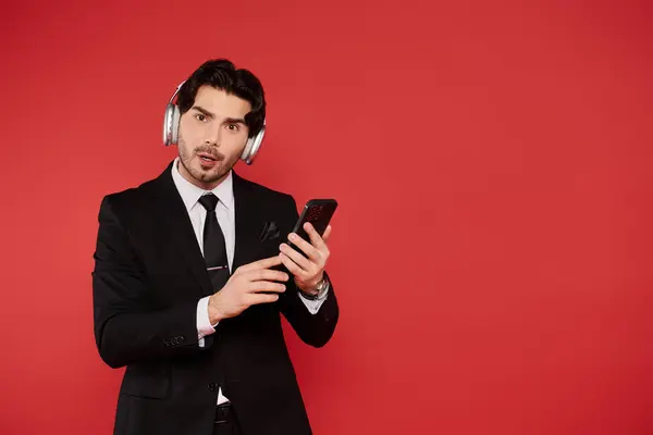 A young handsome man in a suit listens to music with headphones while engaged with his smartphone. — Stock Photo