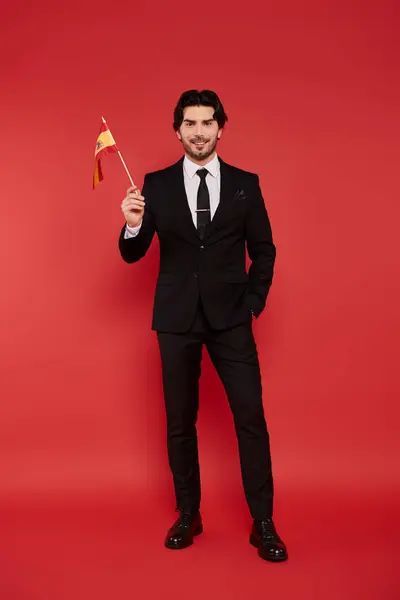 Un giovane con un abito elegante mostra con sicurezza una piccola bandiera, trasudando fascino e stile.. — Foto stock