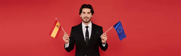 A young man smiles while holding the flags of Spain and the EU. — Stock Photo