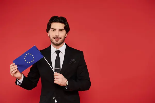 Young man dressed in formal attire displays the EU flag with a confident smile and dynamic energy. — Stock Photo