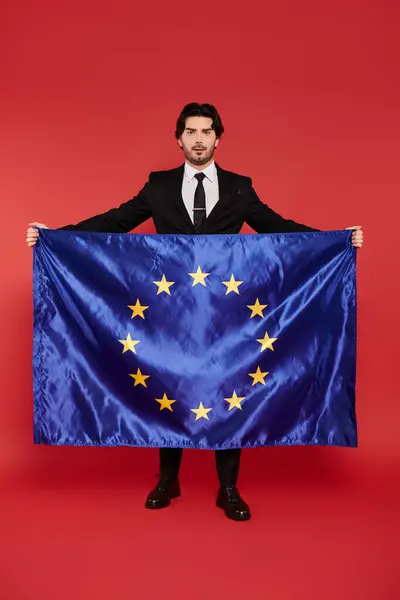 Ein junger, gutaussehender Mann im Anzug hält stolz die Flagge der Europäischen Union in der Hand und demonstriert Einigkeit. — Stockfoto