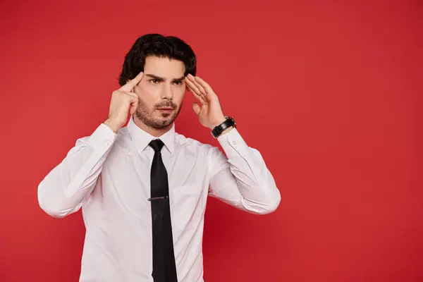 A young, handsome man stands against a striking red background, lost in deep thought. — Stock Photo