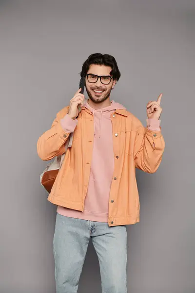Brunette homme avec des lunettes bavarde joyeusement au téléphone à l'intérieur, montrant son style branché. — Photo de stock