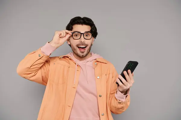 Um homem jovem e bonito com cabelo morena mostra alegria e surpresa ao usar seu smartphone. — Fotografia de Stock