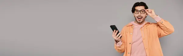 A young man with glasses happily shows his smartphone in a sleek modern interior. — Stock Photo