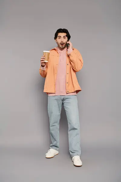Brunette man stands surprised while chatting on the phone and holding a coffee in hand. — Stock Photo