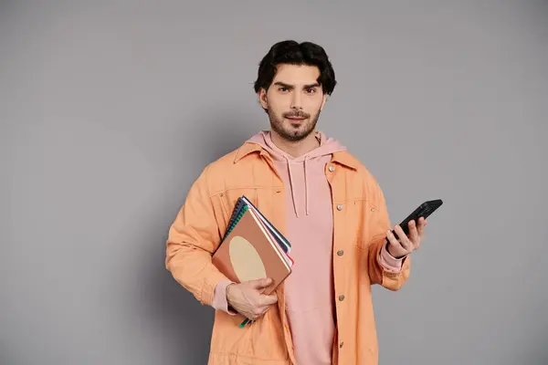 Brunette man casually holds notebooks and a smartphone in each hand. — Stock Photo