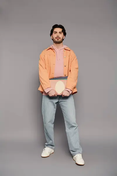 Stylish young man stands confidently, holding a notebook in a studio with a neutral background. — Stock Photo