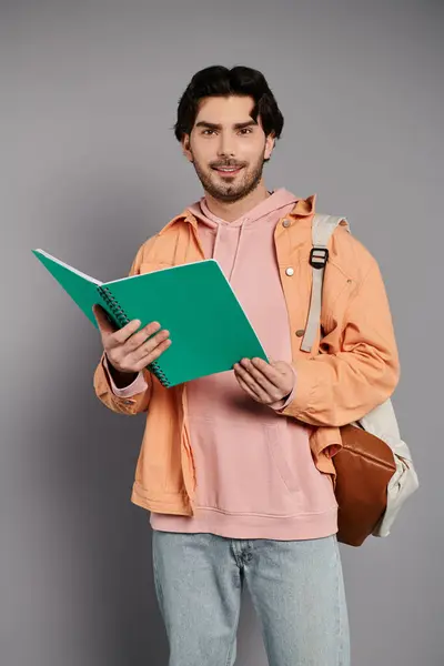 A young, handsome man with brunette hair stands confidently, holding a notebook in his hands. — Stock Photo