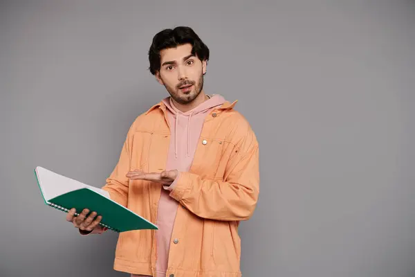 A handsome young man holds a notebook, gesturing expressively in a soft lit room. — Stock Photo
