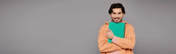 A handsome young man with dark hair and a warm smile embraces a green binder, radiating confidence. — Stock Photo