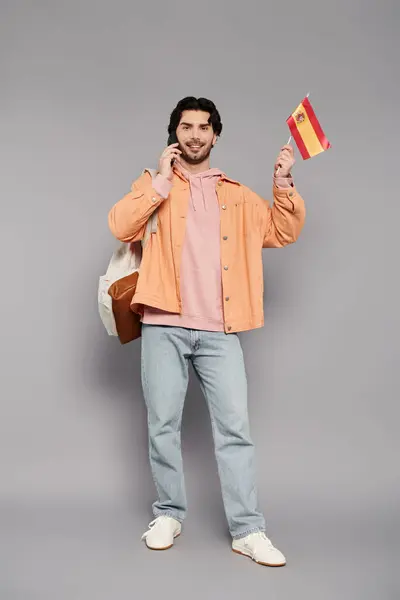Bruna uomo sorride, tenendo una bandiera e chiacchierando al telefono, vestito in abbigliamento casual. — Foto stock