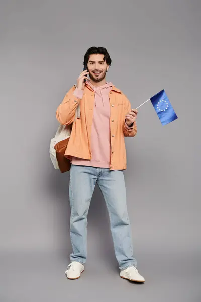 A young man in casual wear smiles cheerfully on the phone while holding a flag. — Stock Photo